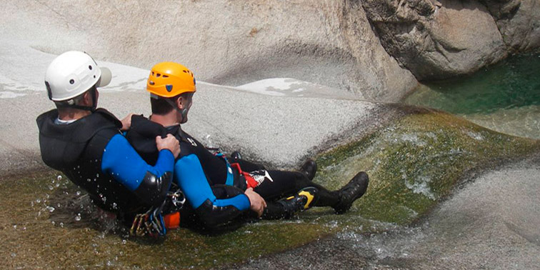 Scène enivrante de canyoning en plein air, deux aventuriers glissant sur une glissière naturelle.