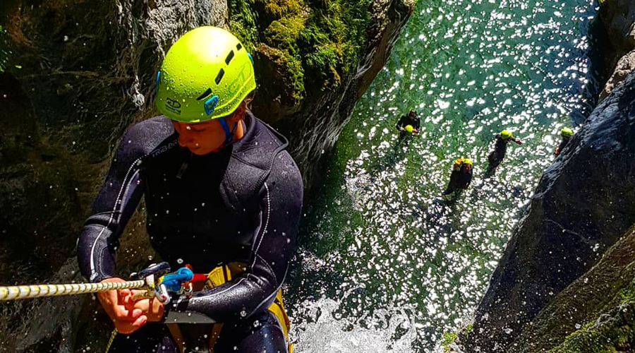 Cette image illustre un moment dynamique de canyoning, montrant un sportif en descente au cœur de la nature, entouré de roches et d'eau vive, évoquant aventure et liberté.