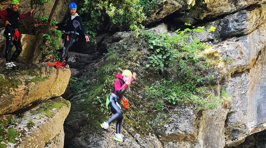 Aventure de canyoning en groupe, sautant des falaises rocheuses vers l'eau cristalline, entouré de nature spectaculaire, illustrant liberté et esprit d'équipe.