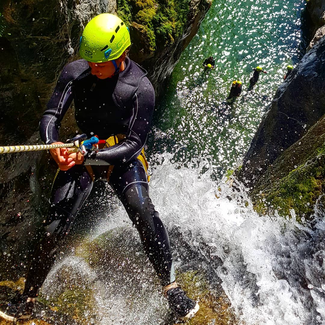 Descente en rappel dans un canyon aquatique avec une combinaison de plongée, casque jaune, et éclaboussures d'eau, soulignant le plaisir et l'intensité de l'aventure.