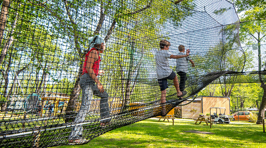 Activités en plein air pour enfants dans un parc d'accrobranche Des enfants s'amusent sur des structures d'accrobranche, entourés de nature, profitant d'une journée ensoleillée avec filets aériens pour une aventure sécurisée et ludique.