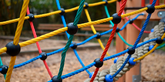 Structure de jeu colorée et sécurisée pour enfants avec un réseau de cordes au parc, favorisant l'exploration et la motricité.