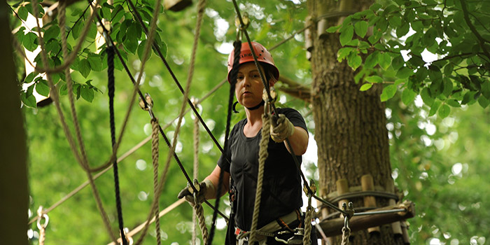 Une aventureuse évolue parmi les arbres en pratiquant l'accrobranche, équipée de sécurité, dans un environnement naturel verdoyant.