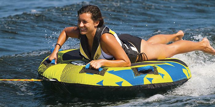 Activité estivale passionnante : une jeune femme sur une bouée tractée, sur les eaux agitées, baignée de soleil et entourée d'éclaboussures, illustre l'esprit d'aventure nautique.