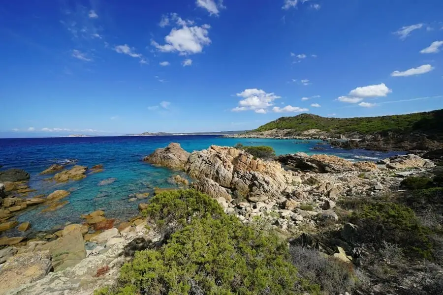 camping-les-orangers-cote-sauvage-corse Vue panoramique sur les rochers et l'eau turquoise d'une crique sauvage près du camping Les Orangers en Corse.